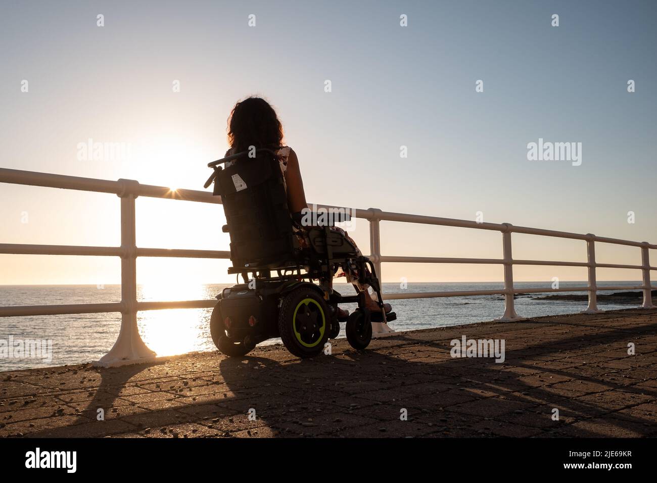 Attractive woman in an electric wheelchair gazing out to sea at sunset ...