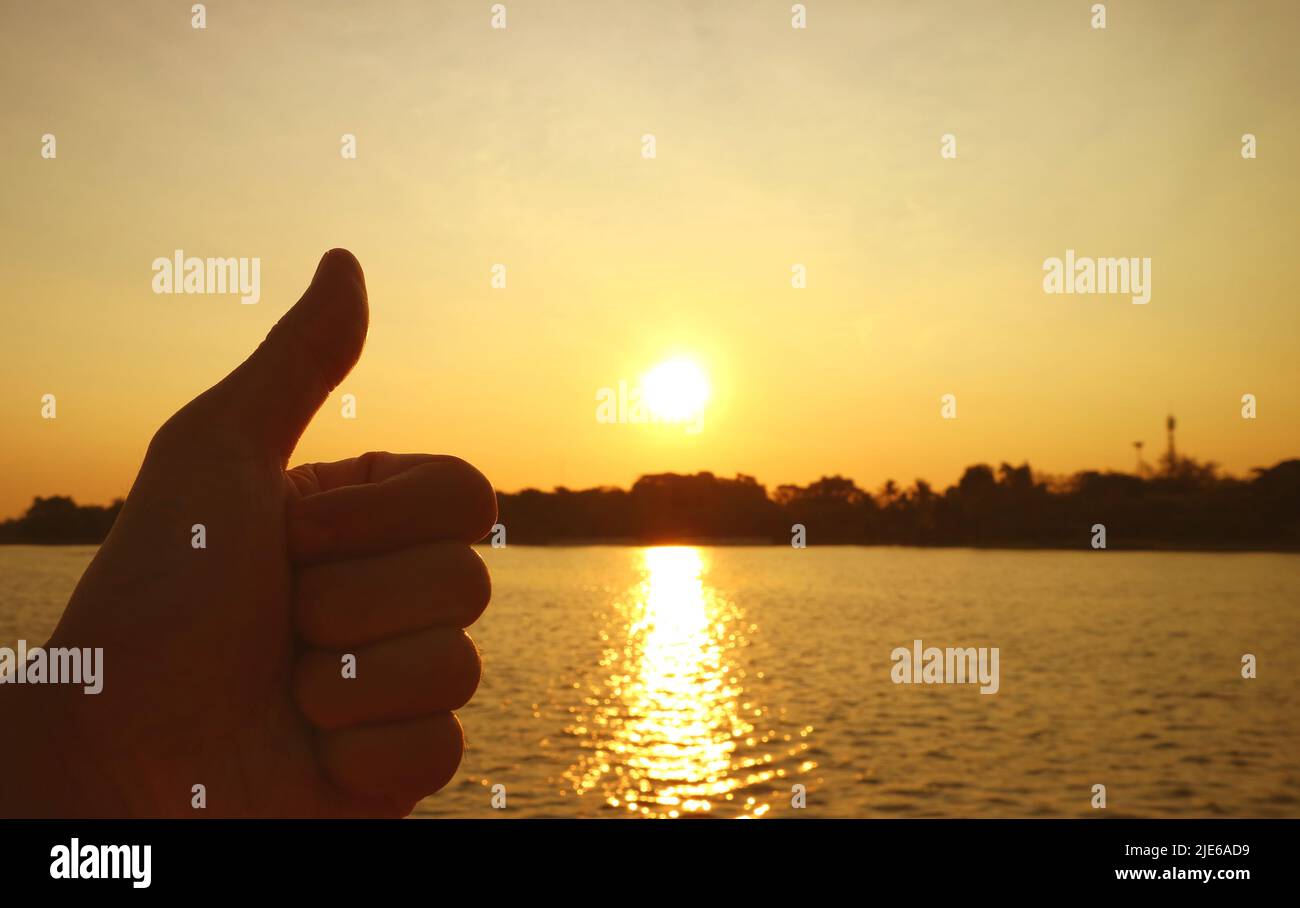 Silhouette of a hand with thumb up on rising bright sun background ...