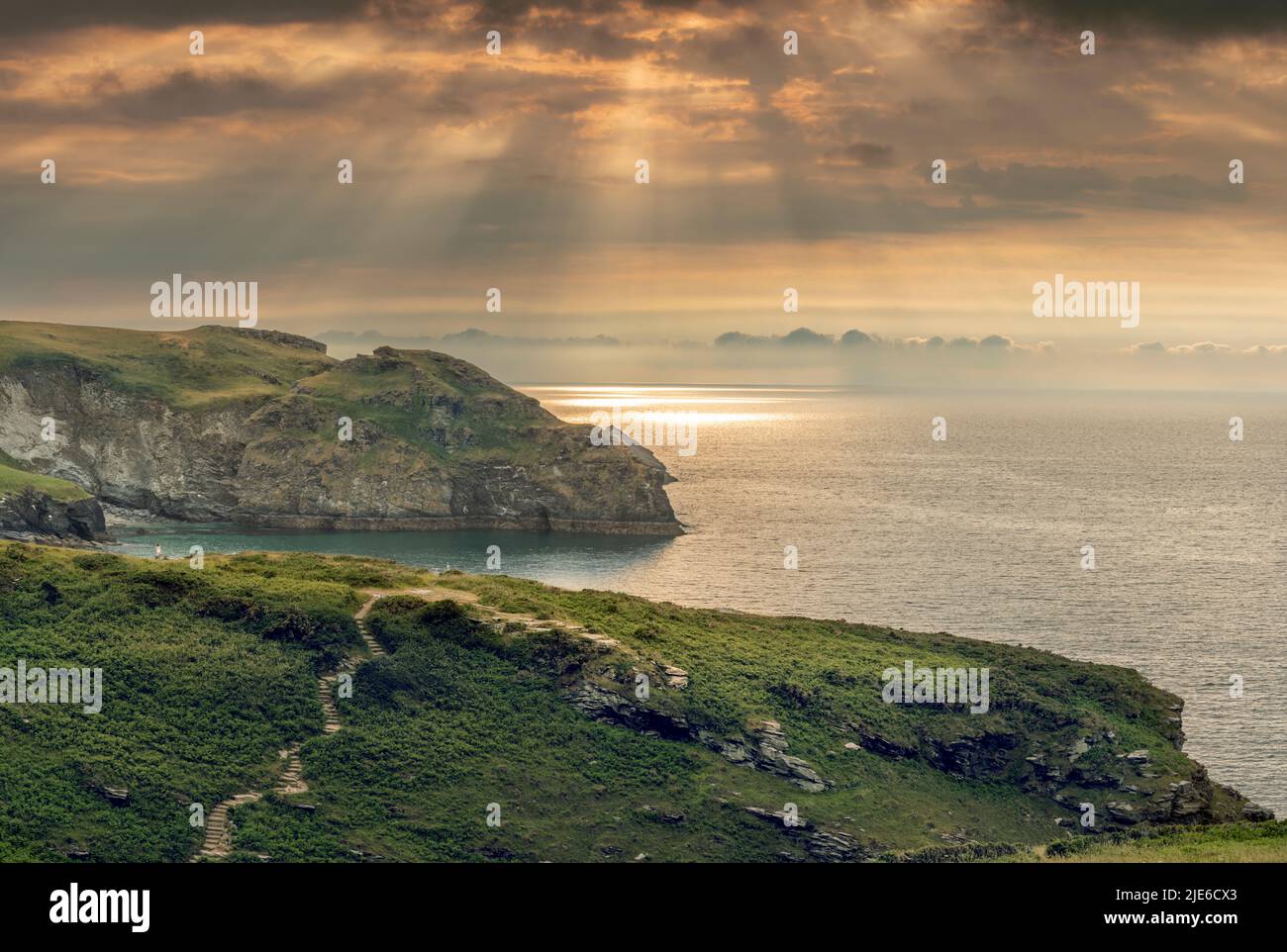 The sea shimmers as the sun breaks through the clouds over the coastal footpath and Rocky Valley at Trethevy near Tintagel in North Cornwall. Stock Photo