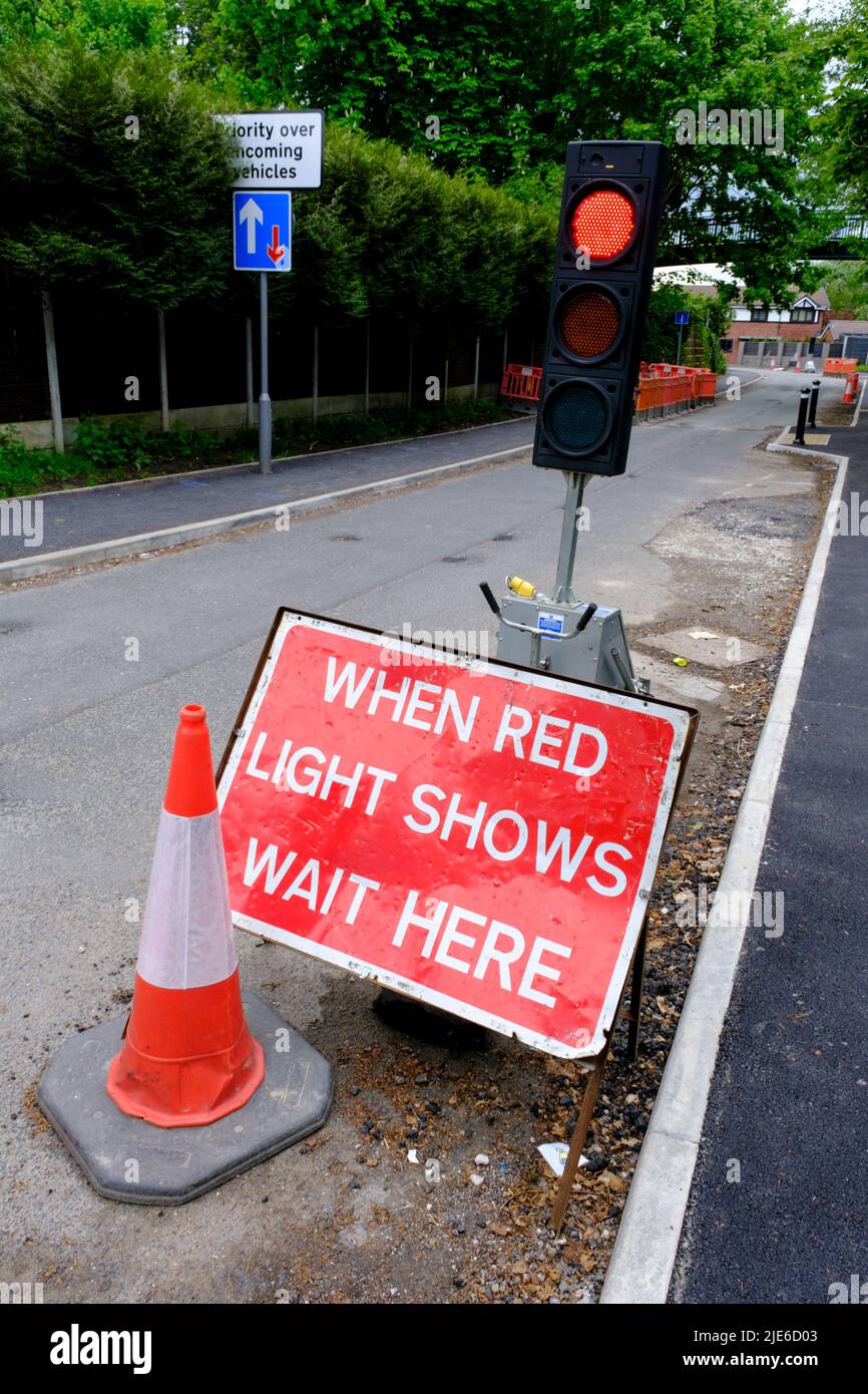 Red warning sign on UK road 'When red light shows wait here' next to temporary traffic light Stock Photo