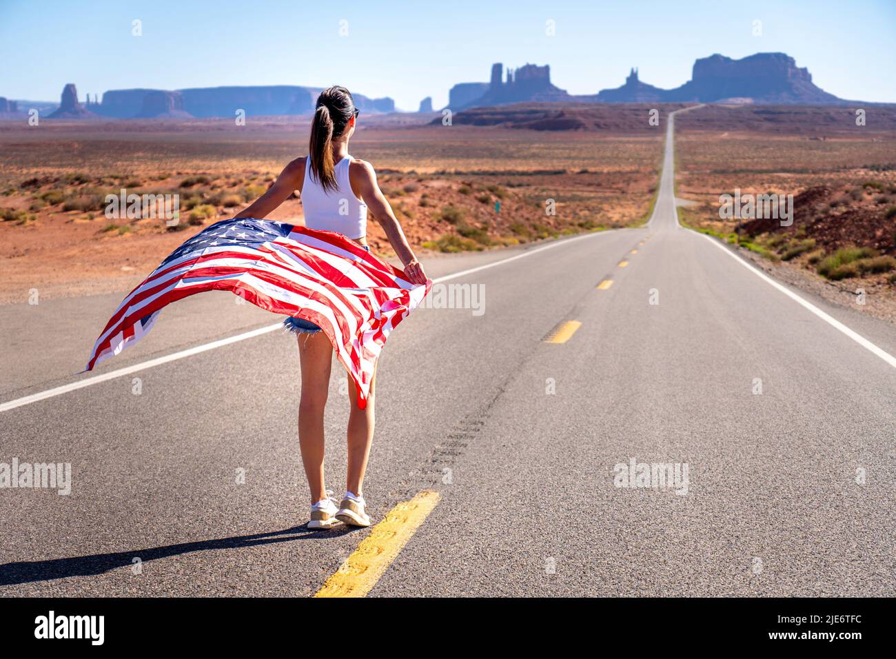 Unknown brunette girl from behind in Monument Valley holding a United States of America flag, wearing short jeans and a white tank top Stock Photo