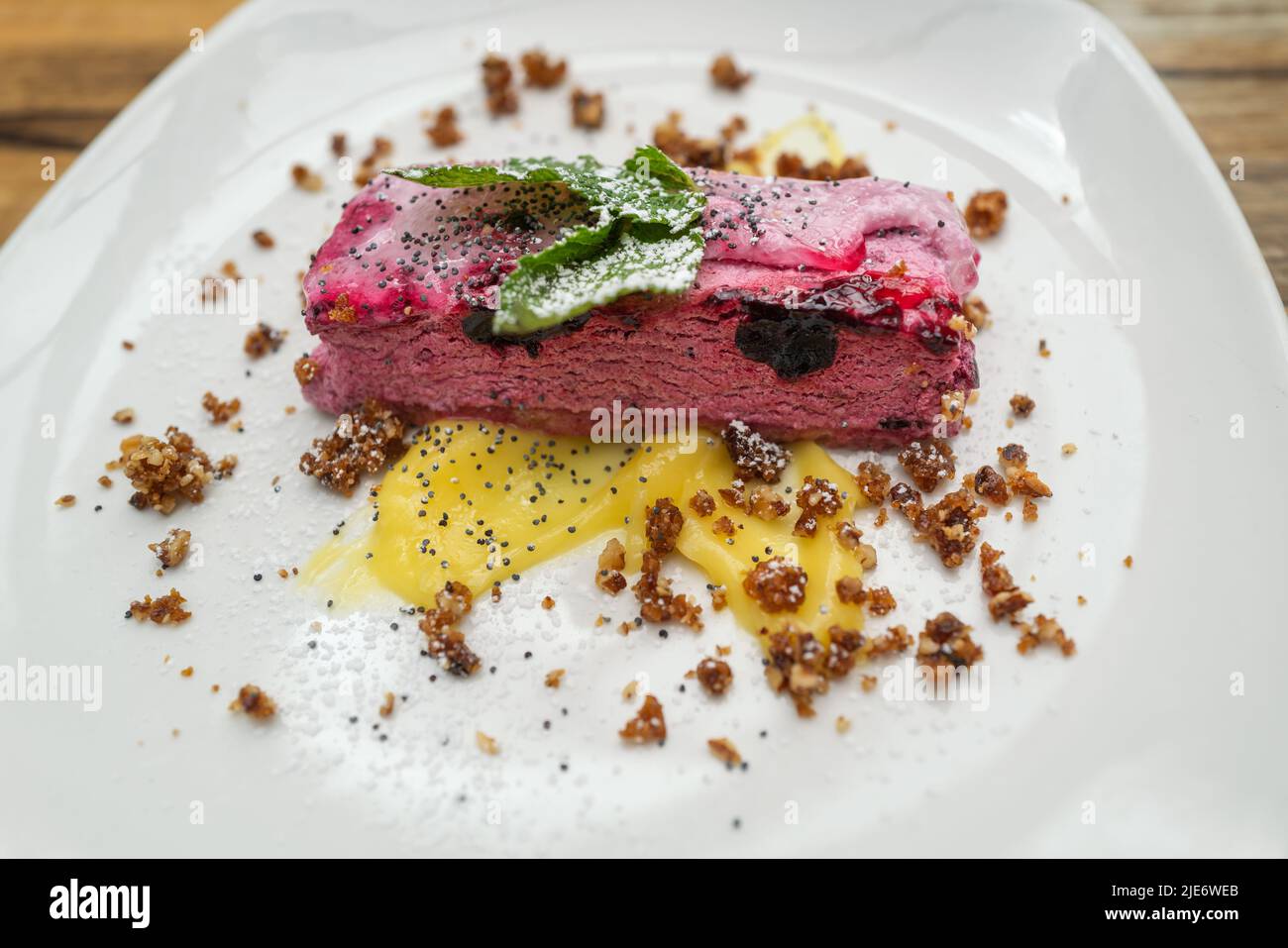 Blackcurrant mousse on a biscuit base with lemon curd and caramelised pecan crumb on a white plate. Stock Photo