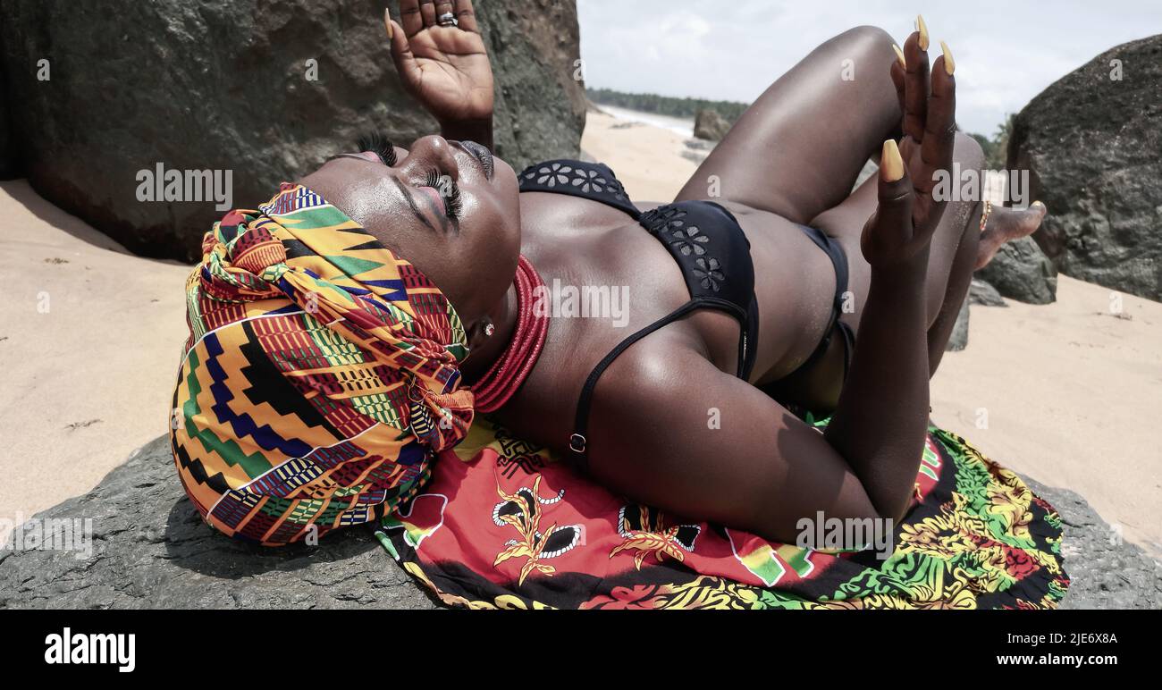 Ghana woman on the beautiful beach of Axim and has a headdress in traditional colors from Africa. Stock Photo