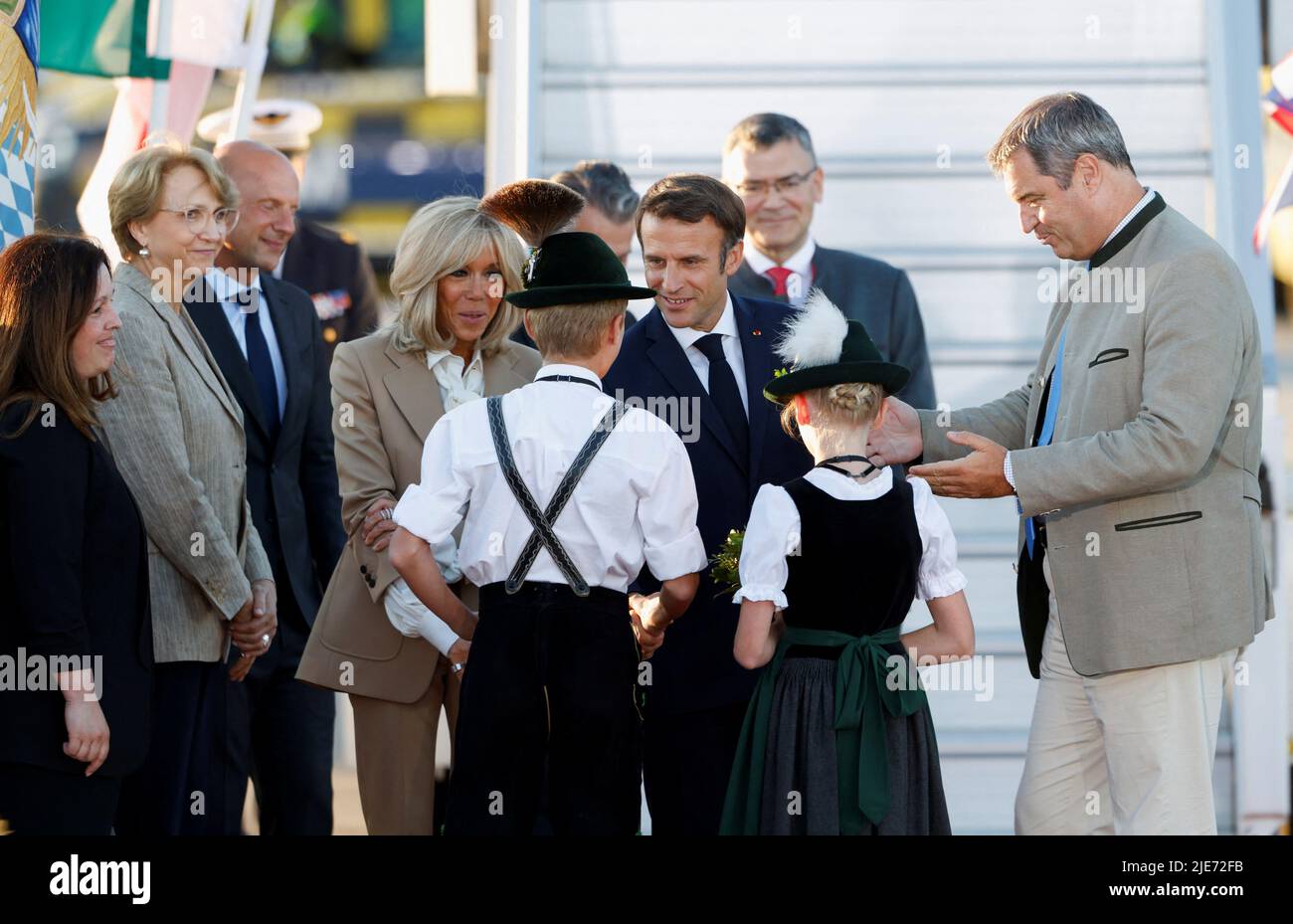 Children in traditional Bavarian clothes welcome French President Emmanuel Macron and his wife Brigitte Macron as they arrive at Franz-Josef-Strauss airport in Munich ahead of the G7 summit, which will take place in the Bavarian alpine resort of Elmau Castle, Germany, June 25, 2022. REUTERS/Michaela Rehle Stock Photo
