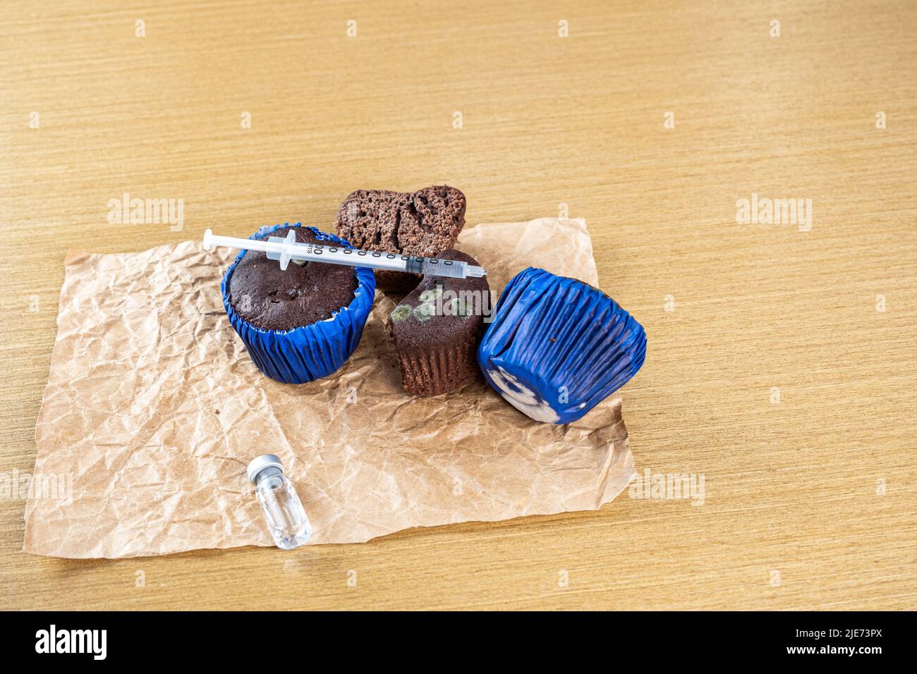 Syringe with insulin over several moldy muffins. Stock Photo