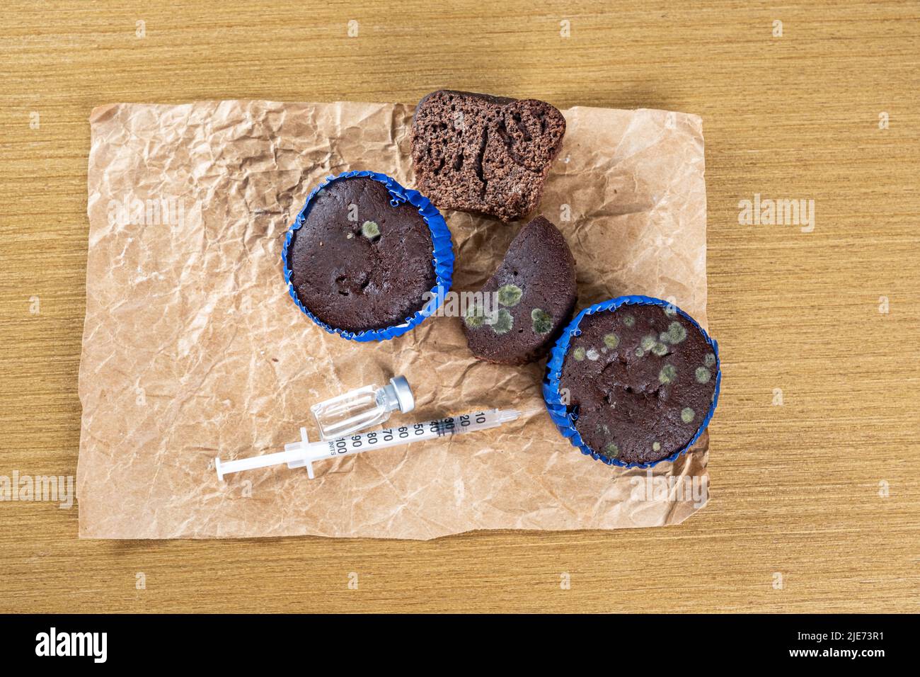Syringe with insulin next to old, moldy muffins top view. Stock Photo