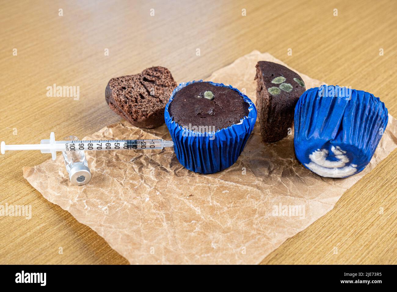 Syringe injecting insulin into moldy chocolate muffin side view. Stock Photo