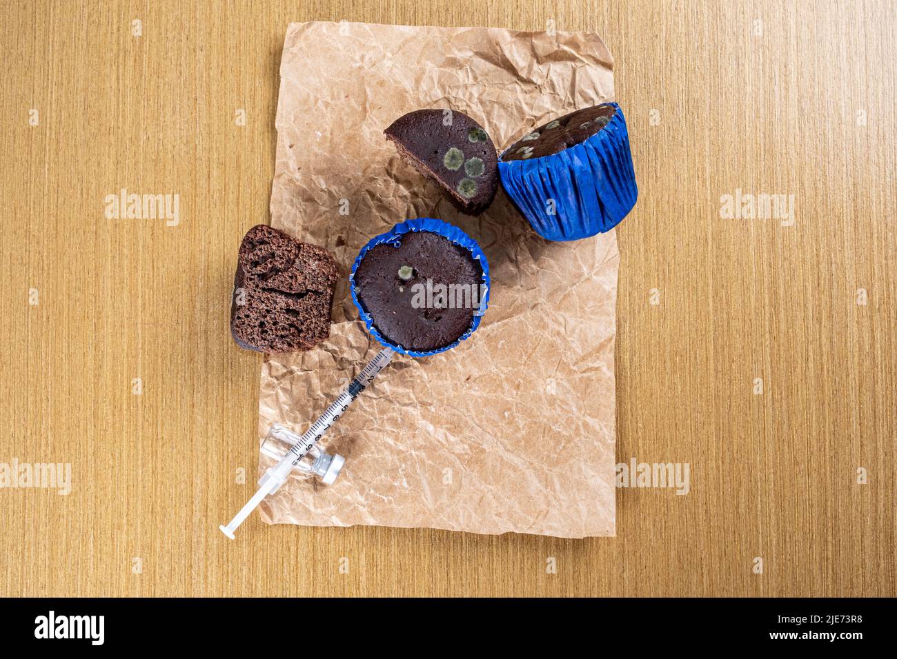 Syringe injecting insulin into moldy chocolate muffin top view. Stock Photo
