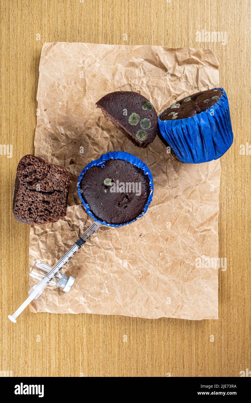Syringe injecting insulin into moldy chocolate muffin top view vertical. Stock Photo