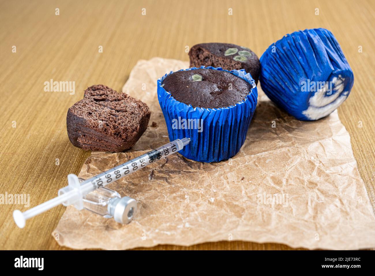 Closeup of syringe injecting insulin into moldy chocolate muffin. Stock Photo