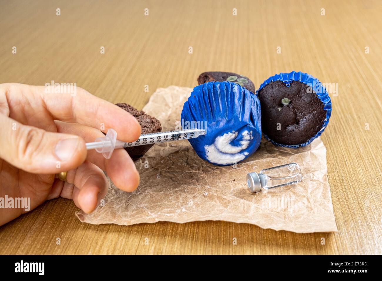 Man with syringe injecting insulin into moldy chocolate muffin side view. Stock Photo