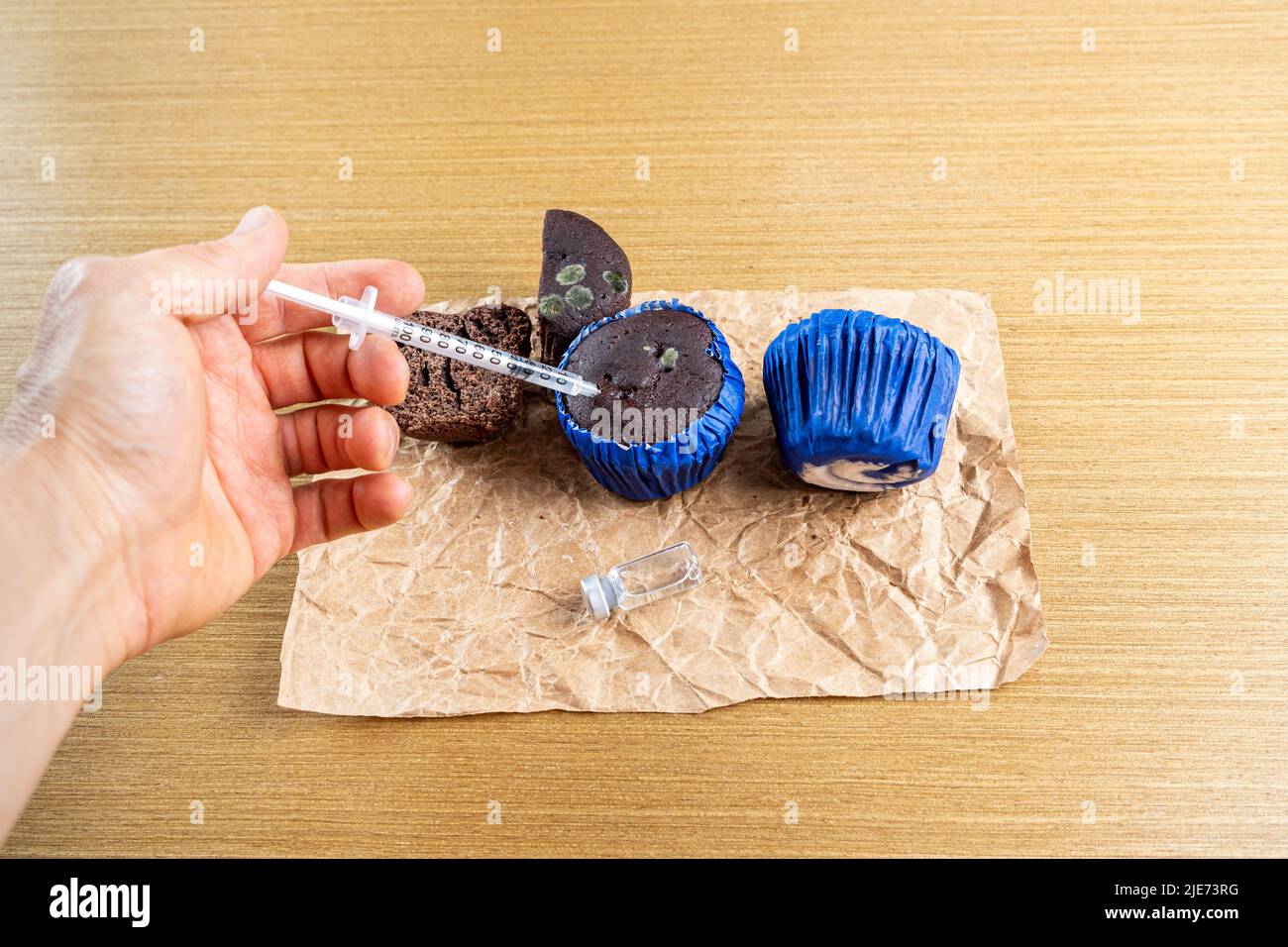 Man with syringe injecting insulin into moldy chocolate muffin. Stock Photo