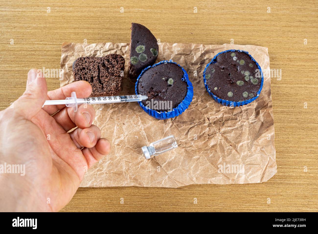 Man with syringe injecting insulin into moldy chocolate muffin top view. Stock Photo