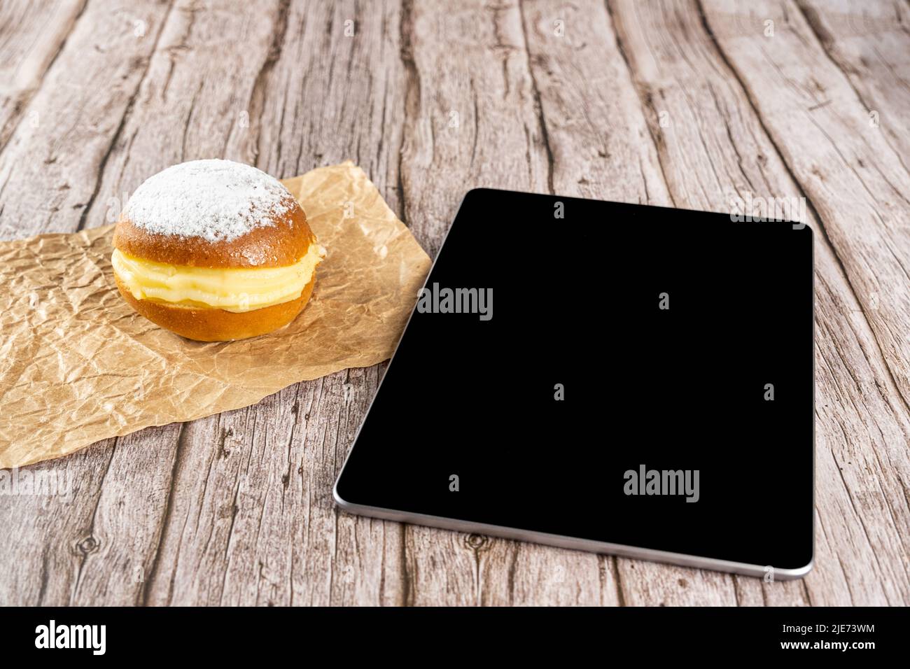 Brazilian cream doughnuts on a brown paper next to a tablet. Stock Photo
