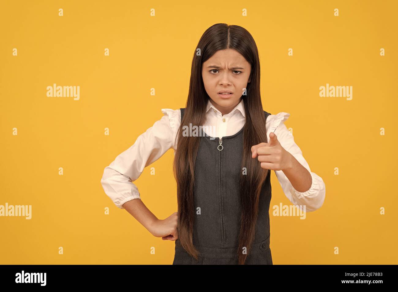 Angry kid in school uniform point accusing finger yellow background, accuse Stock Photo