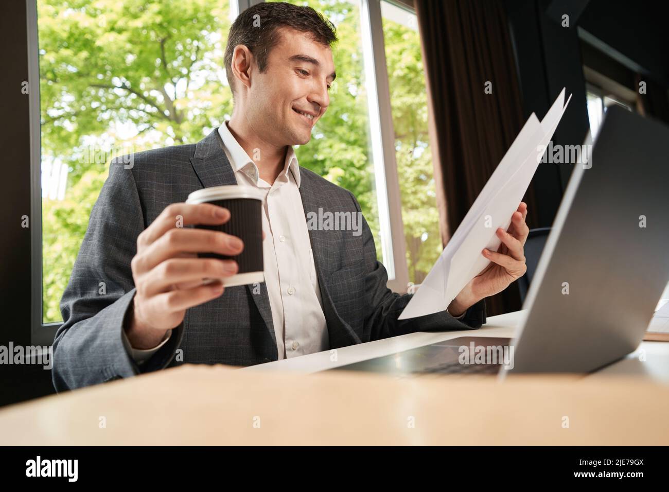 Cheerful clerical worker checking documents while picking coffee cup Stock Photo