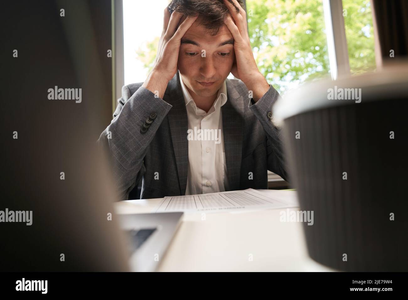 Male grabbing head in despair while looking at spreadsheet Stock Photo