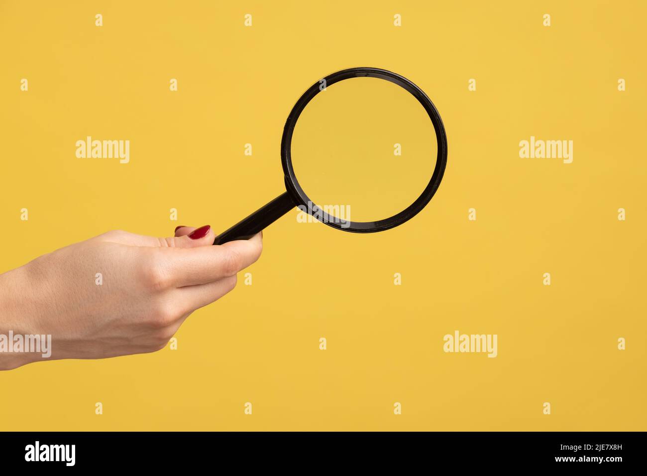 Profile side view closeup of woman hand holding magnify glass, loupe. Indoor studio shot isolated on yellow background. Stock Photo