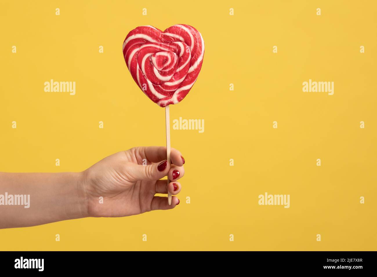 Closeup of woman hand holding appetizing heart shaped candy on stick