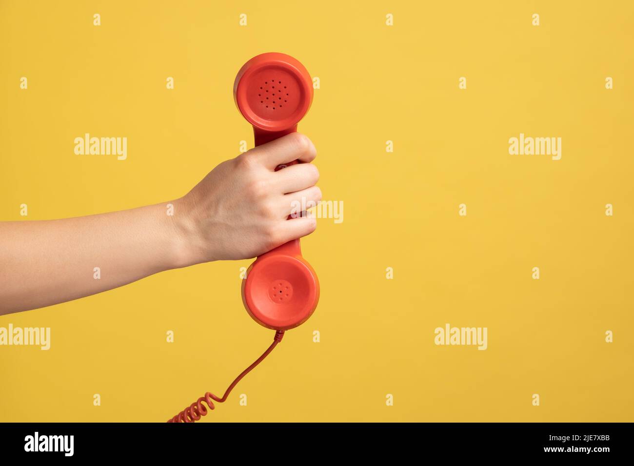 Profile side view closeup of woman hand holding and showing red call telephone handset receiver, call center. Indoor studio shot isolated on yellow background. Stock Photo