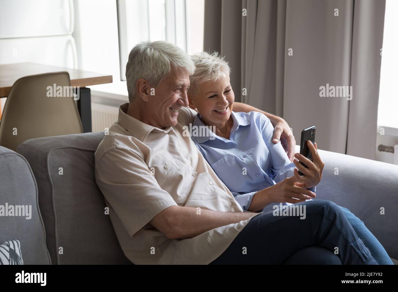 Happy mature couple sit on sofa using modern smartphone Stock Photo