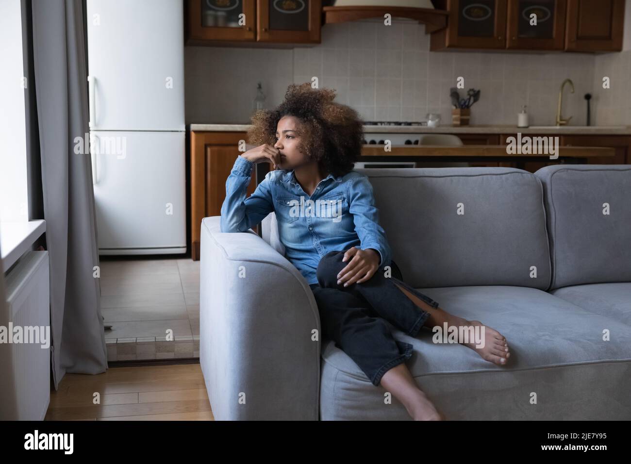Sad African teen girl sit on sofa lost in thoughts Stock Photo