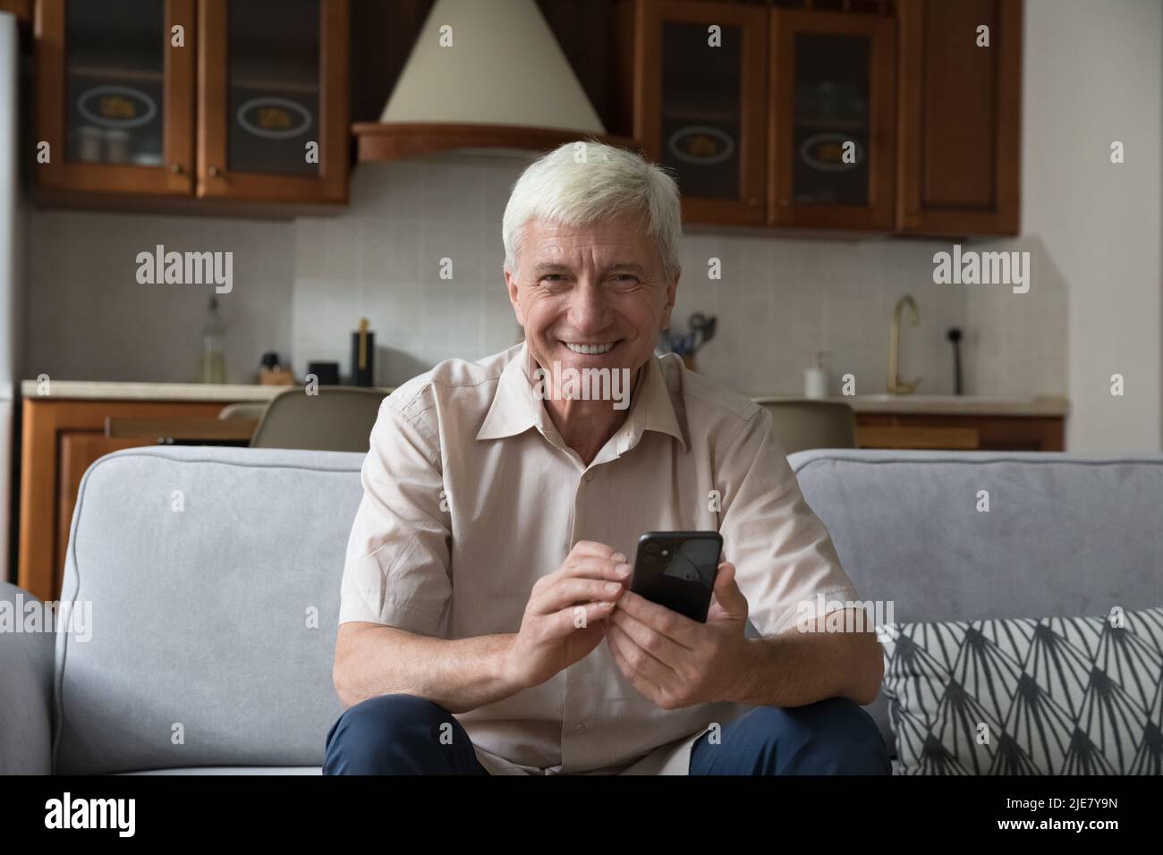 Mature man sit on couch with smartphone looking at camera Stock Photo