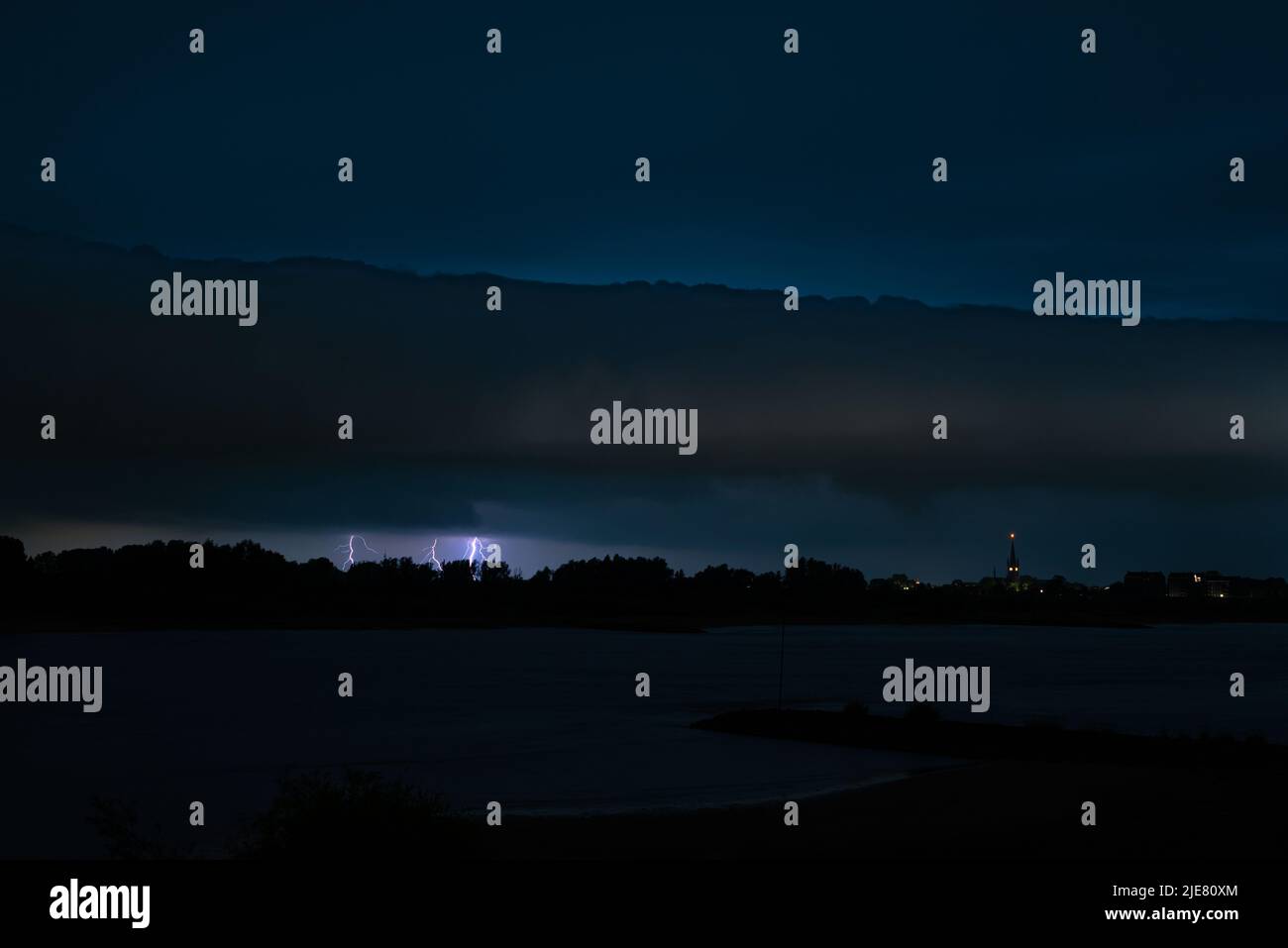 Dramatic sky with an approaching roll cloud with lightning strikes near a river in the night Stock Photo