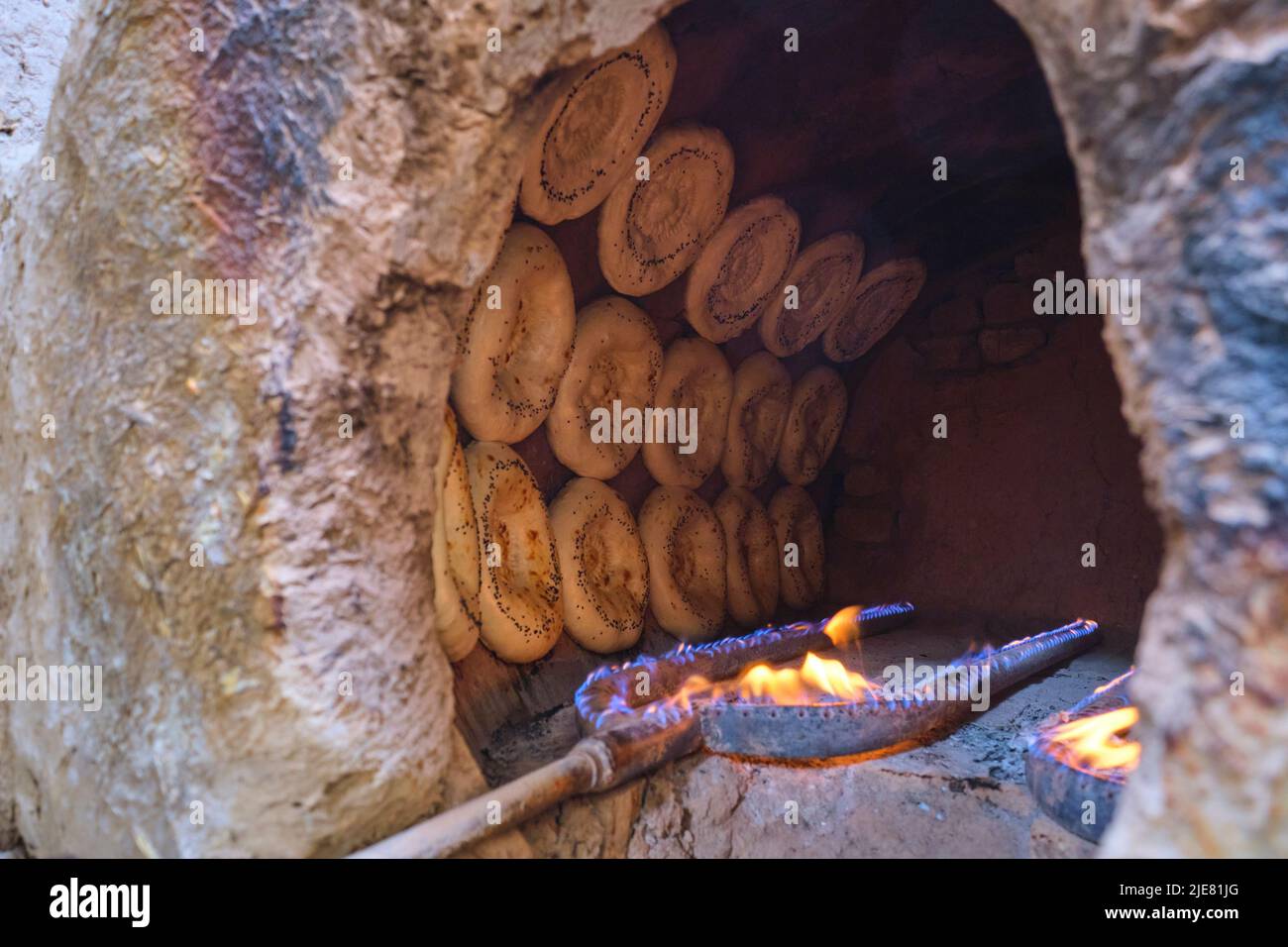 Rows of non bread, stuck to a tandir interior surface, baking. This operation is a typical small, local, hidden behind a house, set up. In Namangan, F Stock Photo