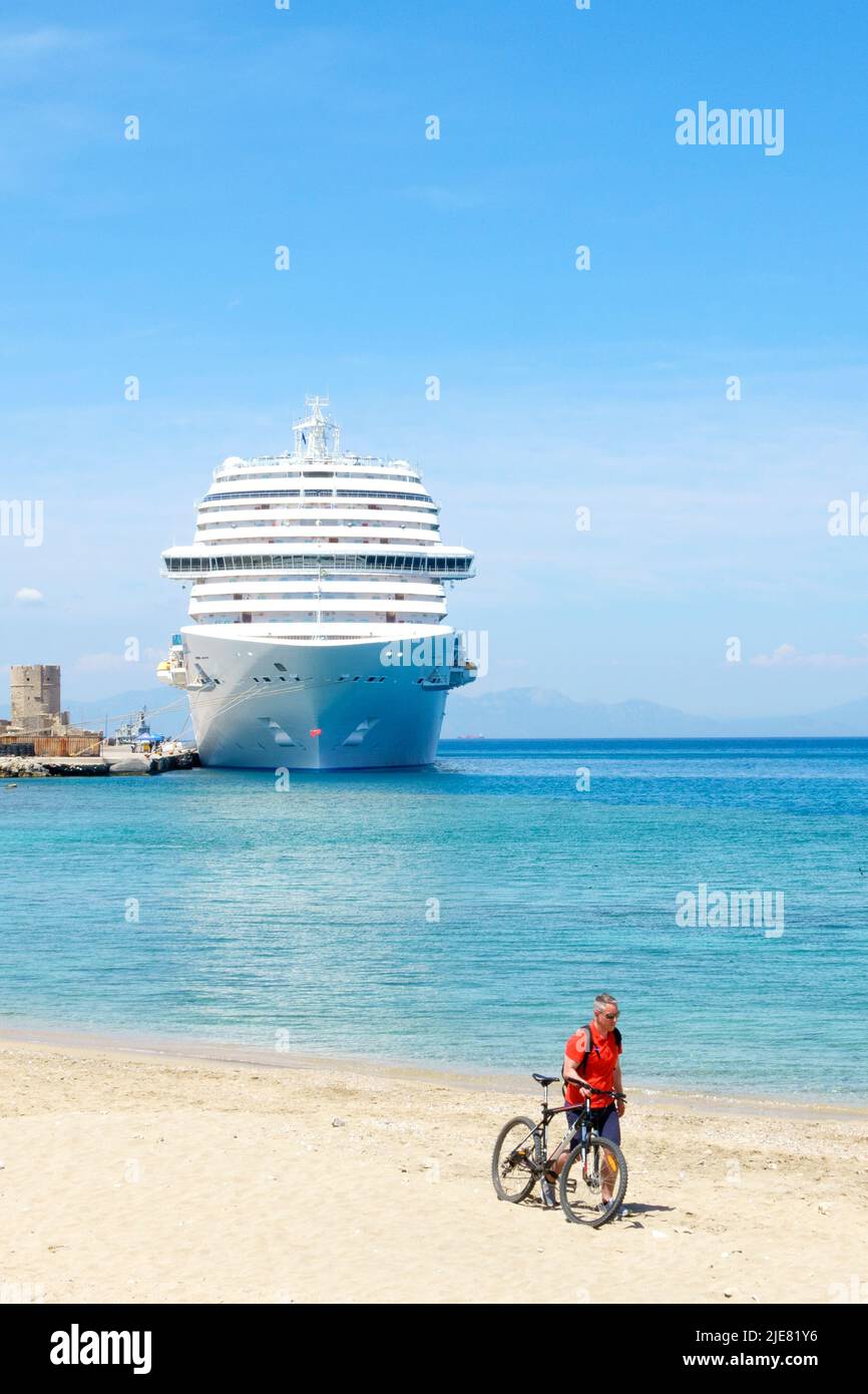 A view across a beach to the Costa Venezia cruise ship moored up in Mandraki Marina during a visit to Rhodes City, Rhodes, Greece Stock Photo