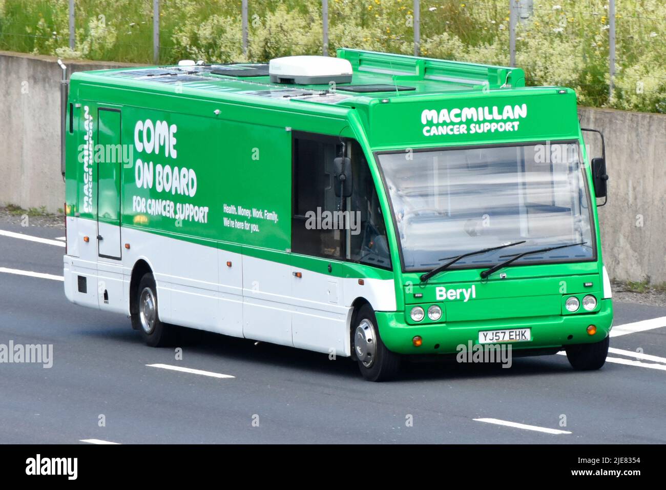 The Macmillan cancer charity & support from a mobile travelling 'Come on Board' help exhibition bus in trademark green driving on UK motorway road Stock Photo