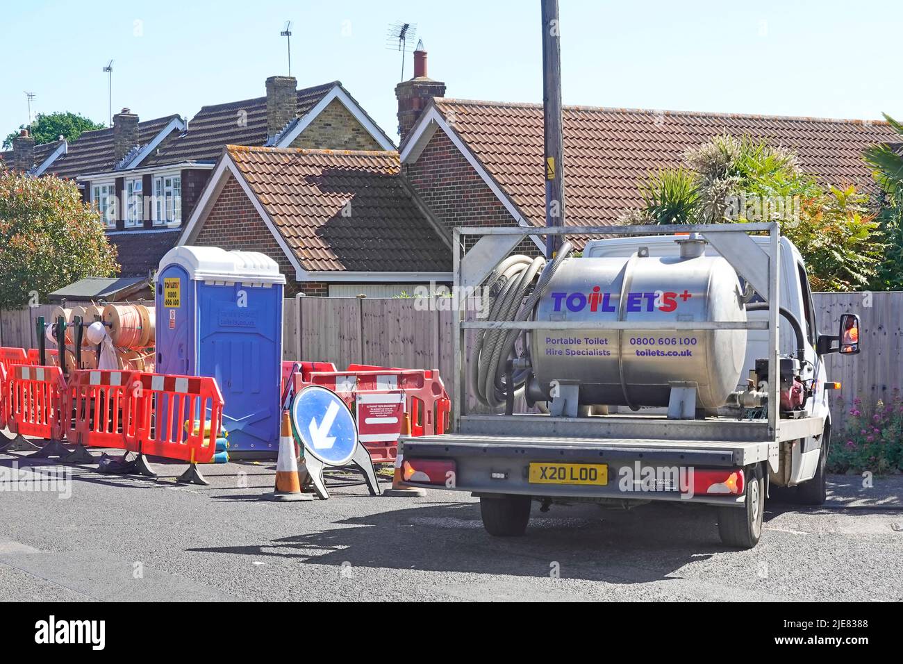 Construction site temporary compound for workers portable blue WC toilet cabin serviced & excrement emptied by pumping hose to tanker lorry truck UK Stock Photo