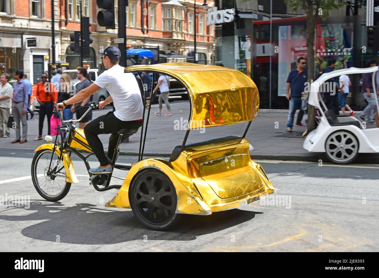 Empty gold colour rickshaw tricycle & driver looking for customers pedalling along London West End Oxford Street shopping and tourist area England UK Stock Photo
