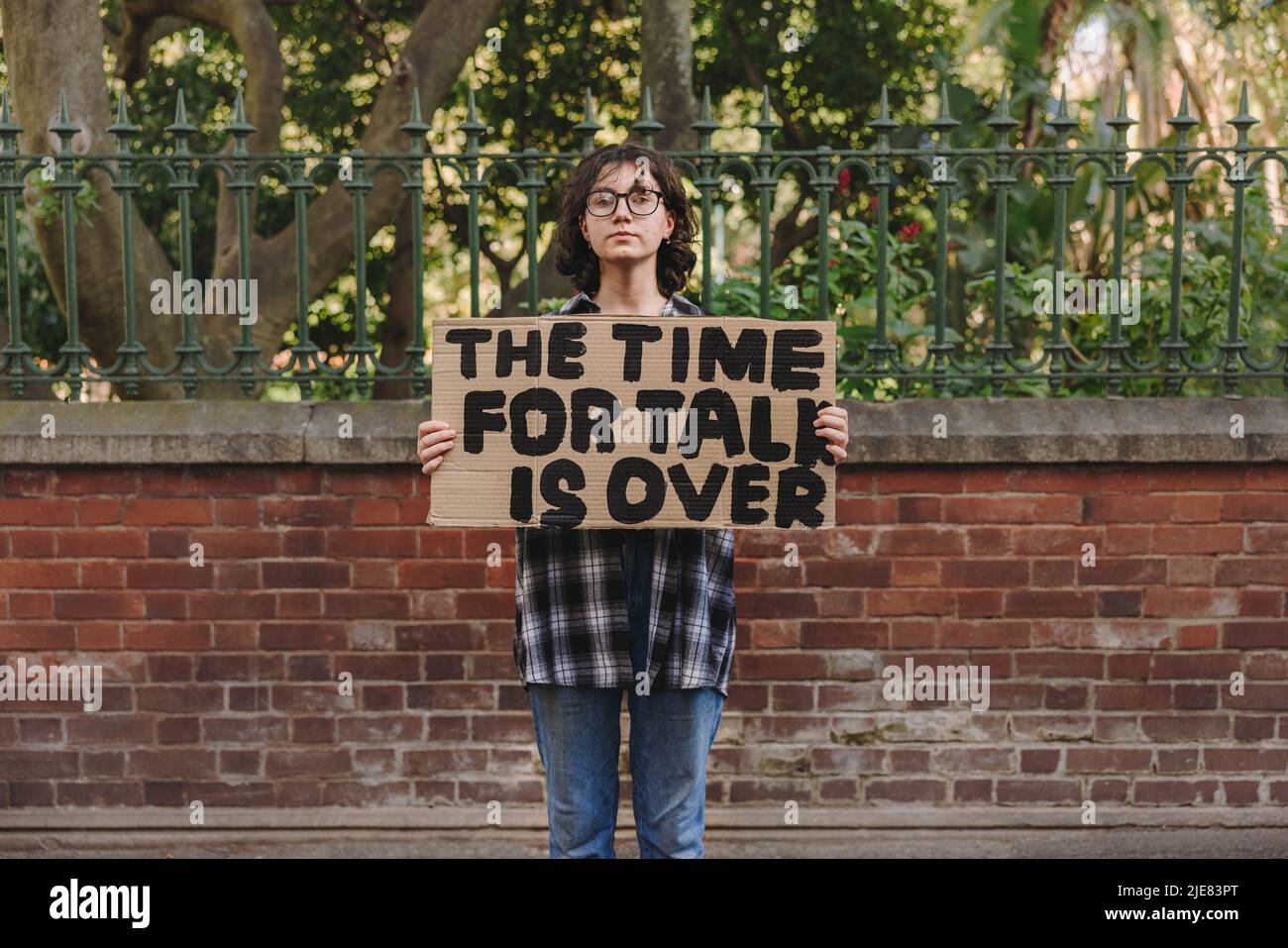 Teenage girl looking at the camera while holding a poster displaying a political message. Youth activist calling for action and change. Stock Photo