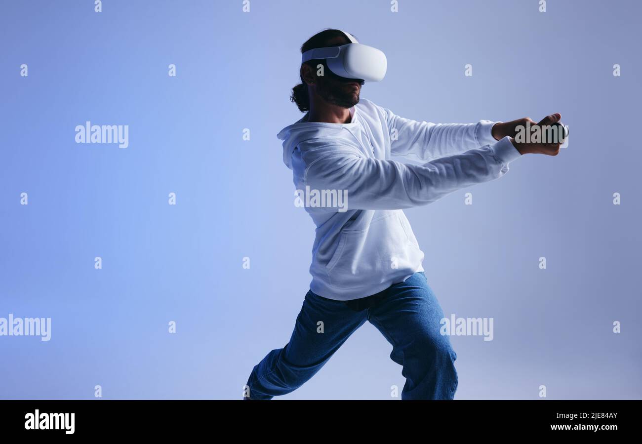 Young man playing cricket in virtual reality. Sporty young man batting a virtual ball using gaming controllers. Active young man exploring immersive V Stock Photo