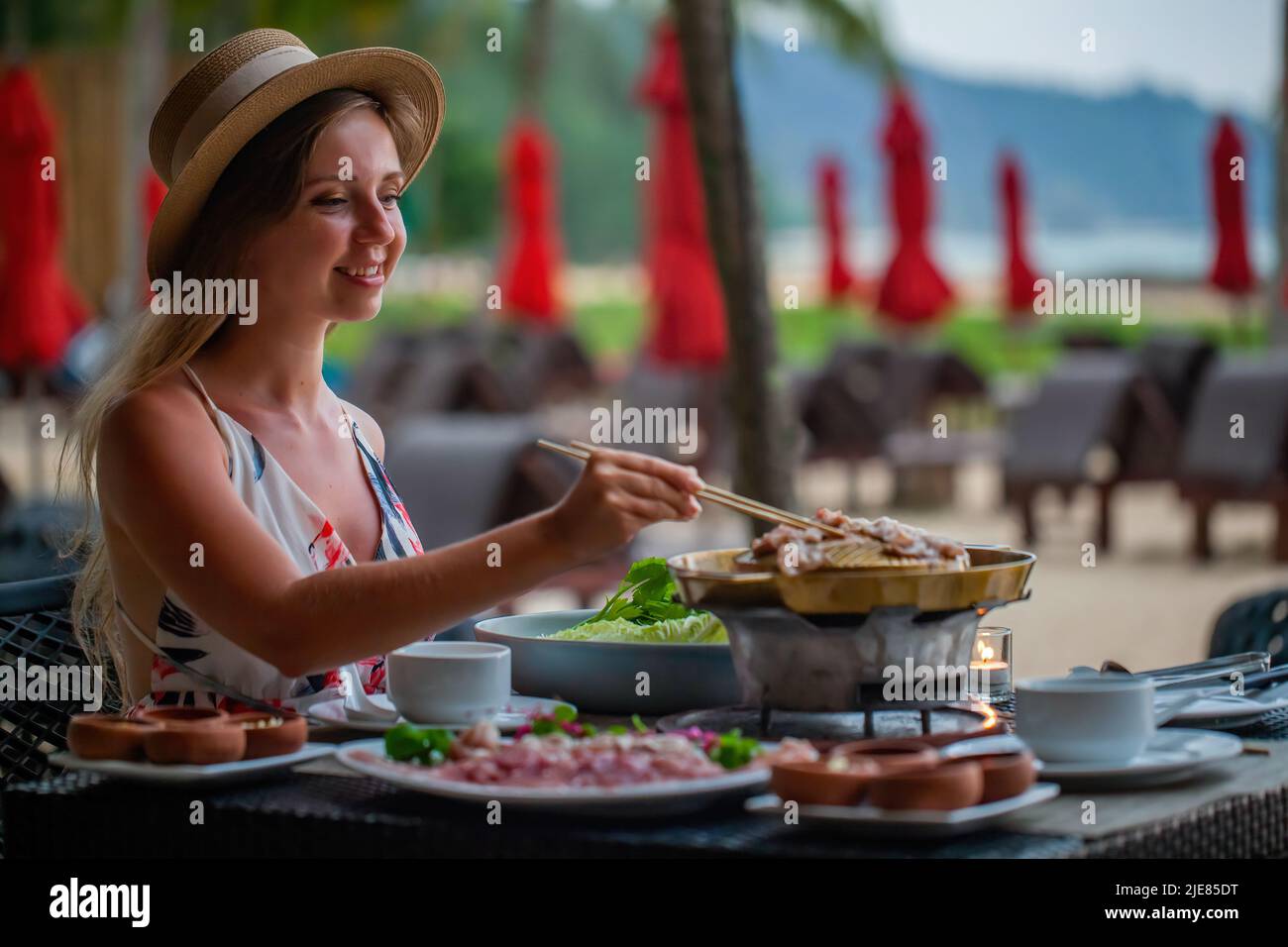 Happy smiling travel woman roasted raw pork slice on Korean barbecue pan. Female traveler cooking Thai style bbq, enjoy eating, grilling pork meat on Stock Photo