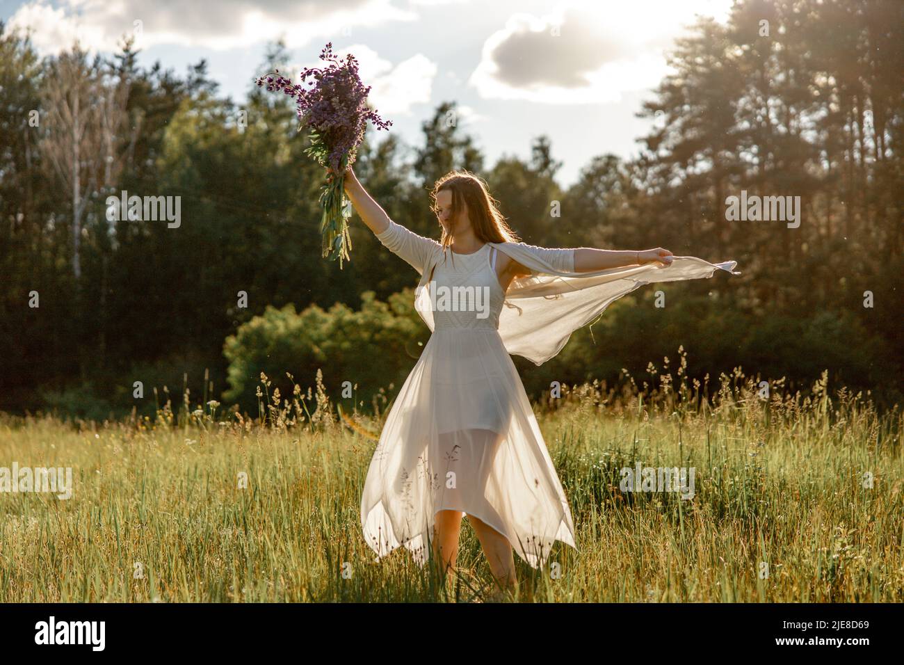 Young beautiful woman, wearing white dress, holding flowers and dancing