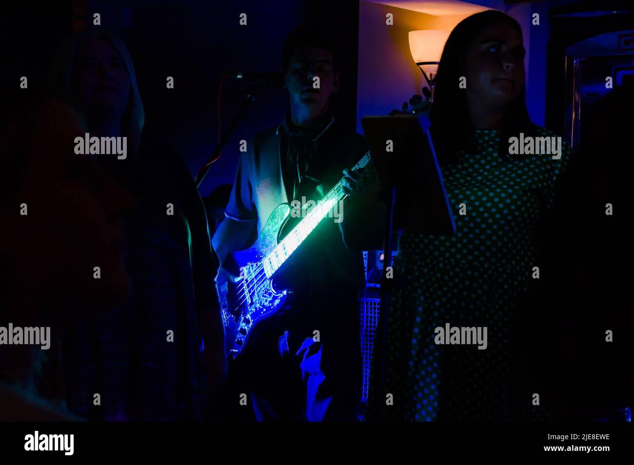 A Musician in The Sub Tones playing a guitar lit with blue & green light at a pub gig Stock Photo