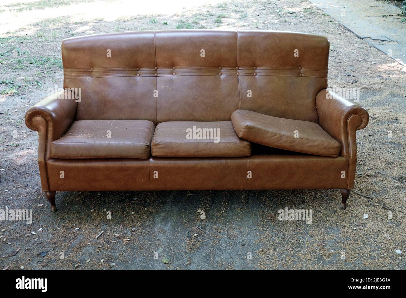 Old vintage brown leather sofa abandoned in a park Stock Photo