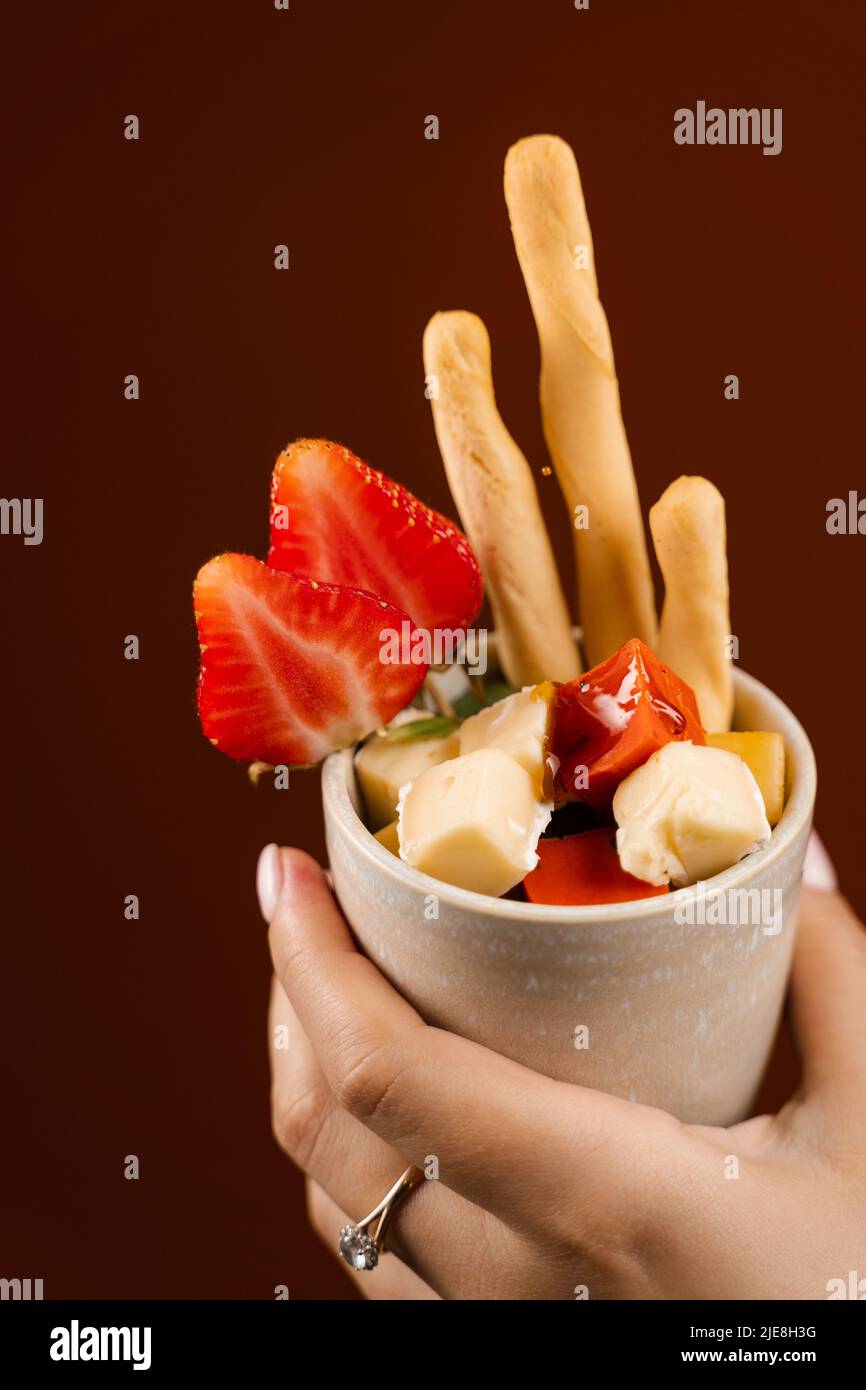 Creative mix of cheeses, grissini sticks and strawberry in cup ...
