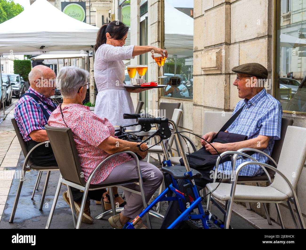 Three elderly people sitting on bar terrace being served with drinks - Tours, France. Stock Photo