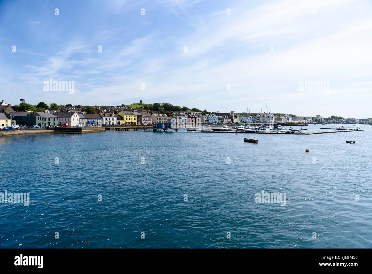 Picturesque Portaferry harbour with several colourful boats moored in the calm water, and traditional buildings lining the waterfront under a clear blue sky, County Down, Northern Ireland.