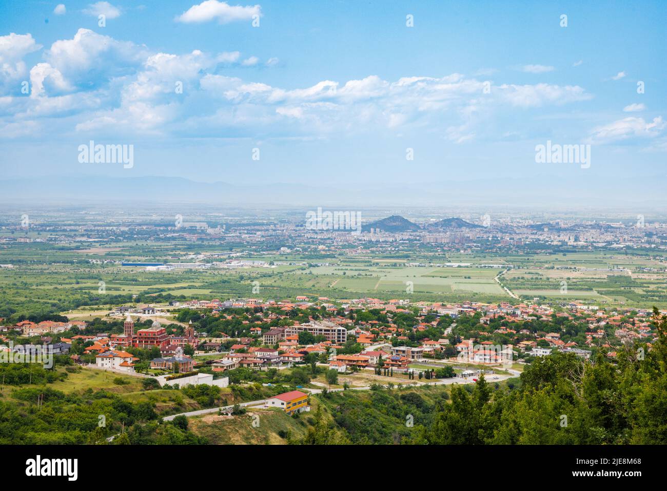 Ancient intermountain town Plovdiv with old residential houses and farm green fields, against backdrop of Rhodope Mountains and hills covered with eve Stock Photo