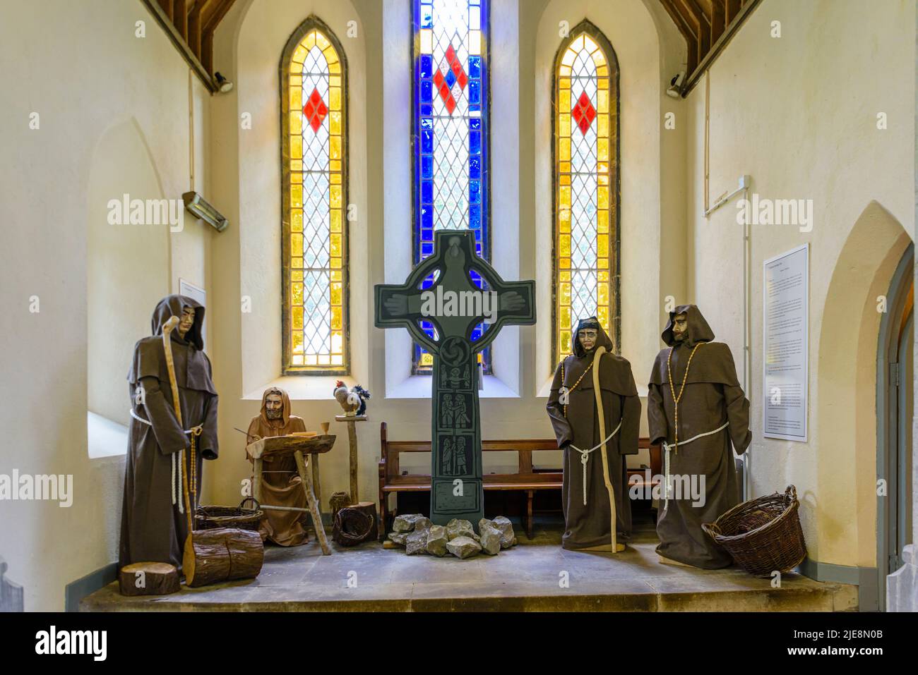 Mannequins dressed as monks around a celtic cross inside a church building. Stock Photo