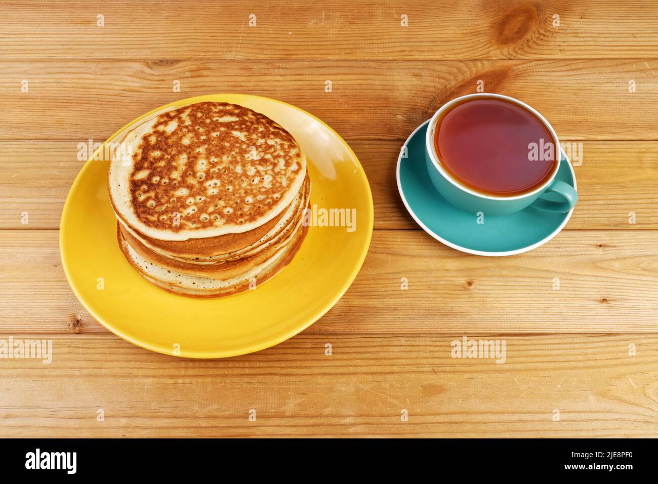 Homemade pancakes in a yellow plate and a cup of tea on a wooden table Stock Photo