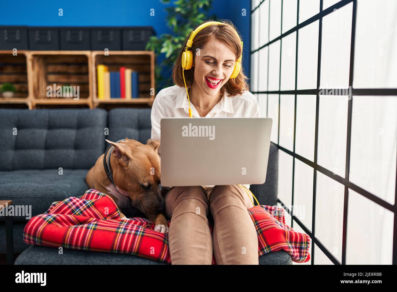 Young beautiful woman using laptop sitting on the sofa looking positive ...
