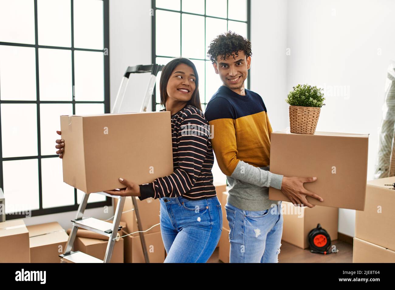 Young latin couple smiling happy holding cardboard boxes at new home ...