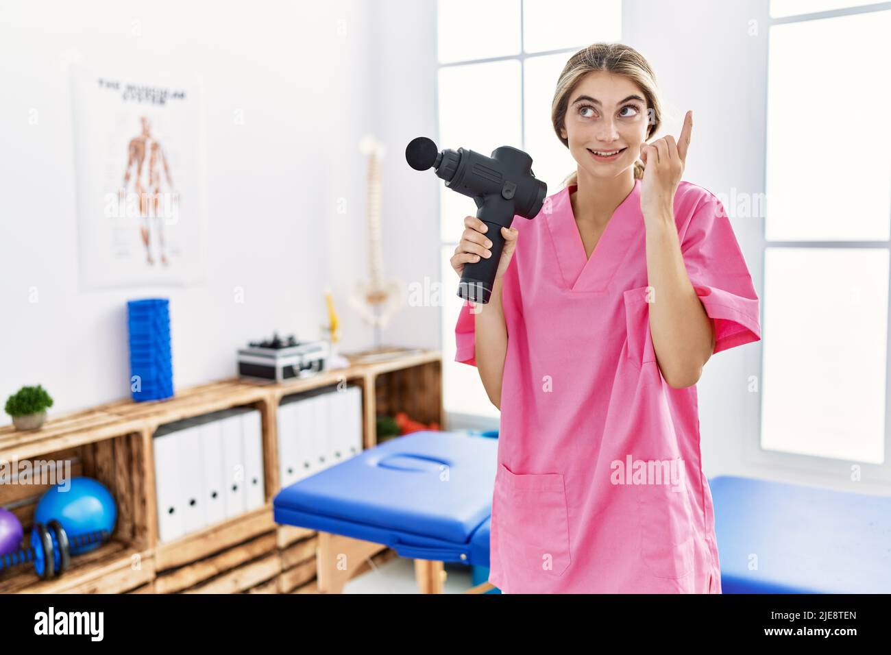 Young physiotherapist woman holding therapy massage gun at wellness