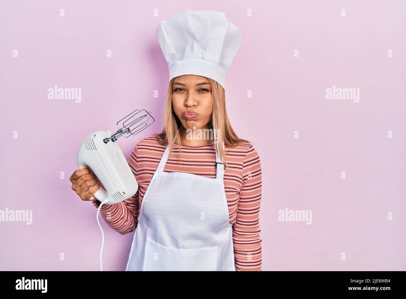 Beautiful hispanic woman holding pastry blender electric mixer puffing
