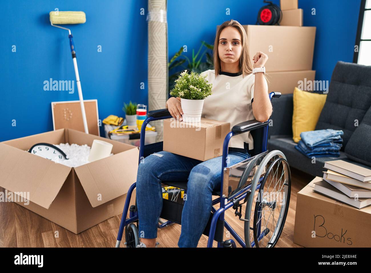 Young woman sitting on wheelchair moving to a new home puffing cheeks ...